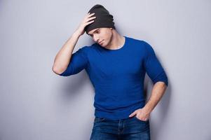 Real macho. Thoughtful young man holding hand on his head while standing against grey background photo