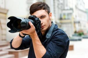 Ready to shoot. Confident young man photographing something while standing outdoors photo