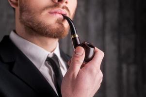 Smoking a pipe. Cropped image of handsome young beard man in formalwear smoking a pipe and looking away photo