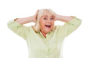 Unbelievable Happy senior woman holding head in hands and smiling while standing isolated on white background photo