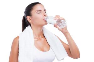 refrescante después del ejercicio. joven cansada sosteniendo una botella con agua y tocándose la frente con la mano mientras estaba aislada en blanco foto