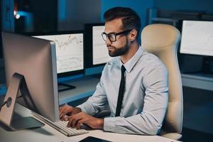 Confident young man working on computer while staying late in the office photo