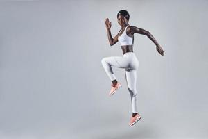 Full length of confident young African woman in sports clothing jumping against gray background photo