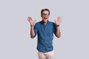 Feeling surprised.  Handsome young man gesturing and keeping mouth open while standing against grey background photo