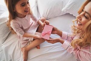 To my princes. Top view of young attractive mother giving a present to her cute little daughter while sitting on the bed at home photo