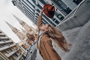 Beauty and style. Attractive young woman holding hat and smiling while spending carefree time in the city photo