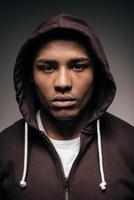 Cool and confident. Confident young African man in hooded shirt looking at camera while standing against grey background photo