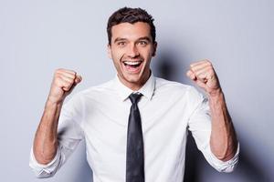 Successful businessman. Happy young man in shirt and tie gesturing and smiling while standing against grey background photo