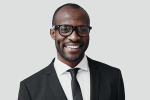 Confident young African man in formalwear looking at camera and smiling while standing against grey background photo