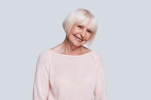 Feeling so happy Beautiful senior woman looking at camera and smiling while standing against grey background photo