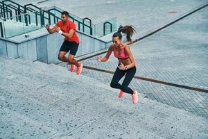 Determined to win young couple in sports clothing jumping on the steps while exercising outdoors photo