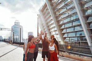 Group of young people in sports clothing encouraging each other while exercising outdoors photo