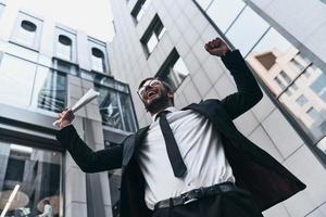 Everything is possible. Low angle view of handsome young man in full suit gesturing and smiling while standing outdoors photo