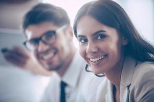 Working together with joy. Close-up part of two coworkers looking at camera with smile while sitting at office photo
