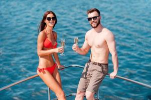 Romantic vacation. Happy young couple holding glasses with champagne while leaning at the handrail on yacht photo