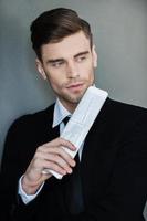 Lost in business thoughts. Thoughtful young businessman holding newspaper and looking away while standing against grey background photo