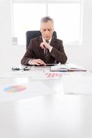 Confident businessman at work. Confident senior man in formalwear working on digital tablet while sitting at his working place photo