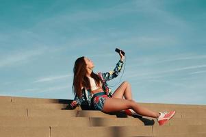 Listening to favorite music. Attractive young woman in sports clothing smiling while sitting on the steps outdoors photo