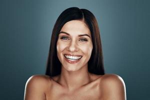 Beautiful young woman smiling while standing against grey background photo