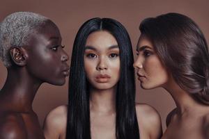 Gorgeous beauties. Three attractive young women looking at camera while standing against brown background photo