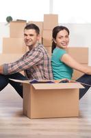 Together in a new house. Beautiful young couple sitting close to each other and smiling while cardboard boxes laying all around them photo