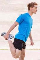 Warming up. Side view of handsome young man doing stretching exercises while standing outdoors photo