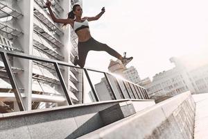 Towards a healthier lifestyle. Full length of modern young woman in sports clothing jumping while exercising outdoors photo