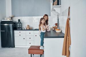 Mother and daughter smiling while preparing something at the kitchen photo