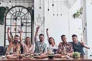 Best friends ever. Beautiful young people in casual wear gesturing and smiling while having a dinner party indoors photo