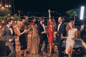 Group of happy people in formalwear dancing and having fun together with confetti flying all around photo