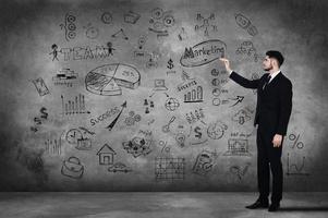 Good strategy is a key to success. Full length of confident young man in full suit sketching on the concrete wall photo