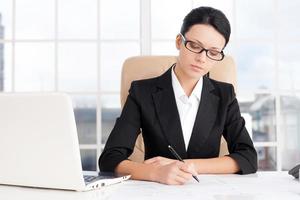 Businesswoman at work. Confident young business writing something on paper while sitting at her working place photo