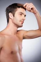 Man combing hair. Side view of handsome young beard man looking at camera and combing his hair while standing isolated on grey background photo