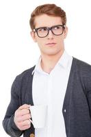 Having a coffee break. Thoughtful young man holding cup of coffee and looking away while standing isolated on white photo