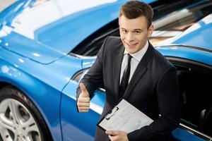 Great choose Top view of handsome young car salesman standing at the dealership with thumb up photo