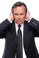 Thick and tired. Tired mature man in shirt and tie covering ears with hands and keeping eyes closed while standing isolated on white background photo