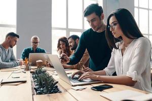 equipo trabajando juntos. grupo de jóvenes modernos con ropa informal inteligente usando tecnologías modernas mientras trabajan en la oficina creativa foto