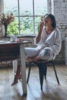 disfrutando de su desayuno en casa. atractiva joven mujer sonriente manteniendo los ojos cerrados y comiendo algunas bayas mientras desayuna en casa foto