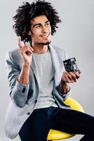 Got an idea for next shoot Handsome young African man holding retro styled camera and looking away with smile while sitting against grey background photo