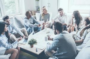 Discussing new project together. Group of cheerful young business people sitting around office desk together and discussing something photo