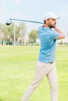 golfista profesional joven confiado jugando al golf mientras está de pie en el campo de golf foto