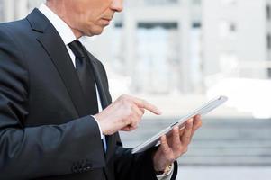 Working on tablet. Side view cropped image of confident senior man in formalwear working on digital tablet while standing outdoors photo