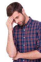 Failed again. Frustrated young man in casual shirt touching his forehead with hand and keeping eyes closed while standing isolated on white photo