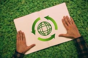 Protect the environment. Top view close-up image of man holding hands on his notebook with arrow and planet symbol at moss background photo