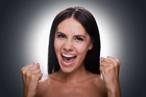 Happiness without limits. Portrait of happy young shirtless woman looking at camera and gesturing while standing against grey background photo