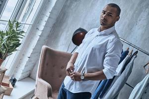 estilo y carisma. apuesto joven africano abotonándose la camisa mientras está de pie en casa foto