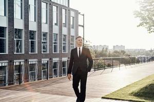 Confident mature businessman walking near office building outdoors photo