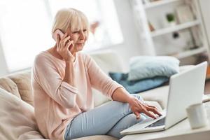 Happy to talk with nearest. Beautiful senior woman talking on her smart phone and smiling while relaxing on the couch at home photo