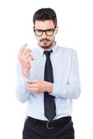 Used to success. Confident young man in shirt and tie looking at camera and adjusting his sleeve while standing against white background photo