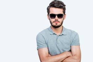 Serious and handsome. Confident young man keeping arms crossed and looking at camera while standing against white background photo